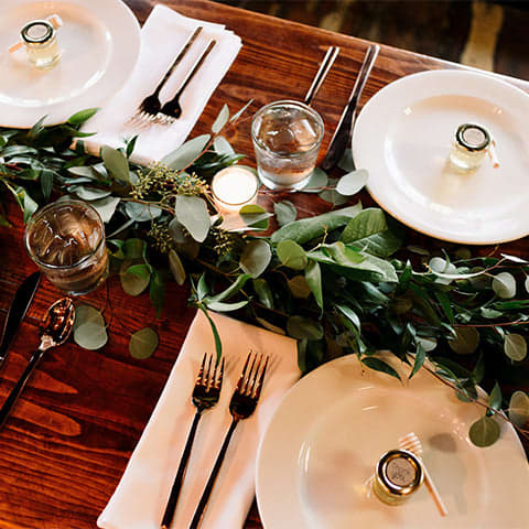 Modern tablescape with white plates and green garland running across the wood table.