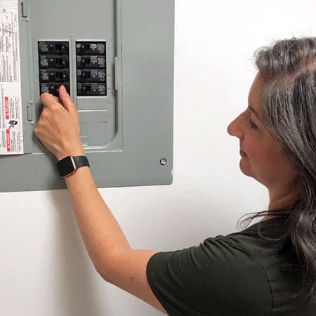 Image of a woman turning off the power using the circuit breaker before removing their ceiling fan.
