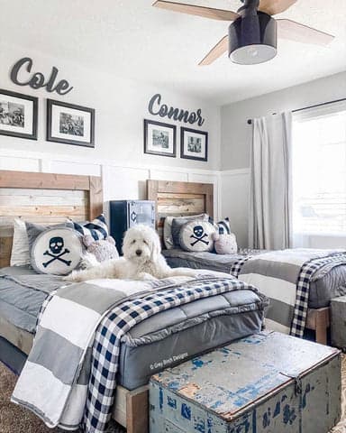 Cute white pup sitting on a bed in a kids room. Matching bed right next to the first bed. There is a Hunter ceiling fan hanging above the beds.
