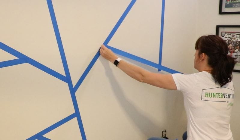 Huntervention team applying painters tape to accent wall